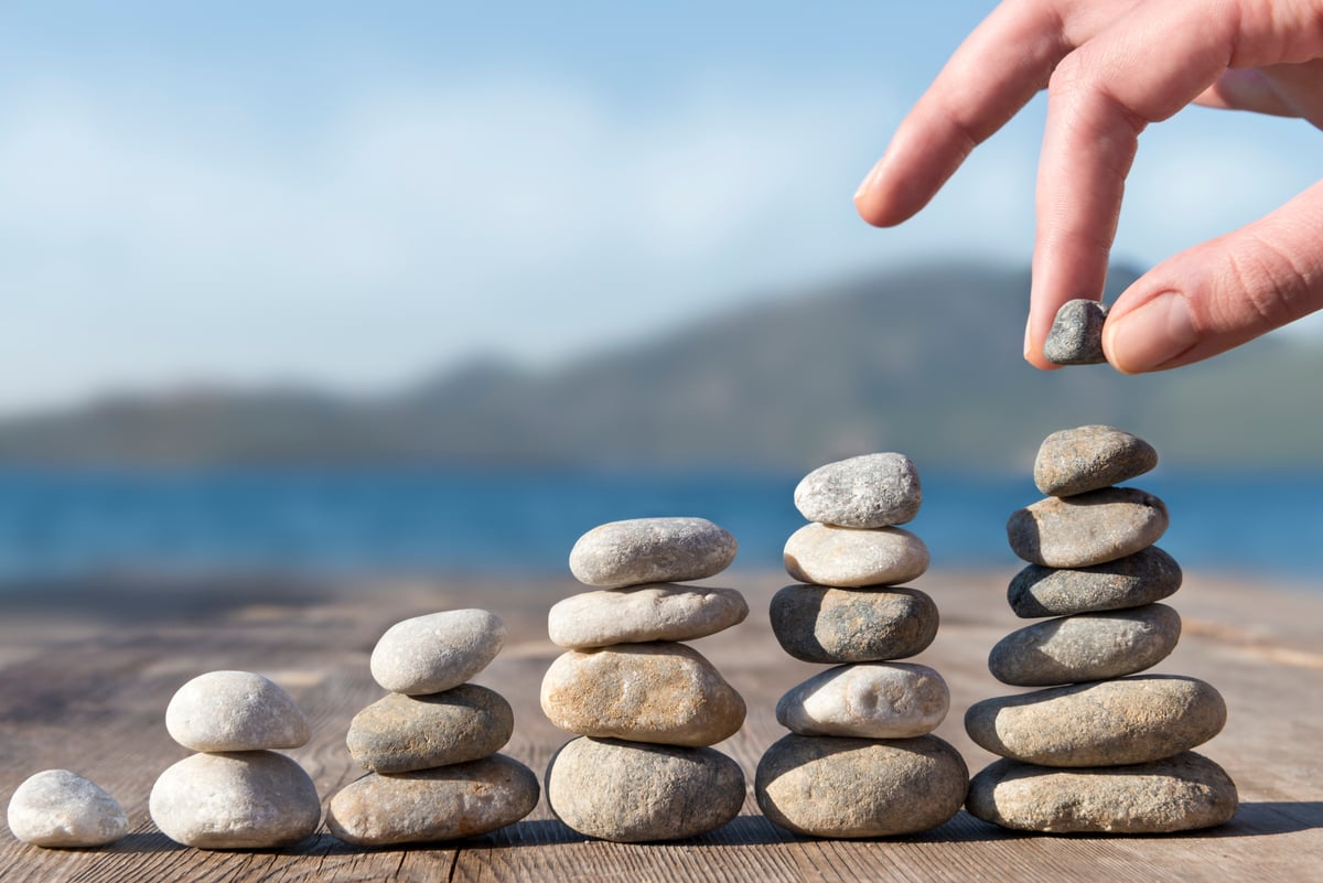 A hand stacking stones in increasingly taller towers.