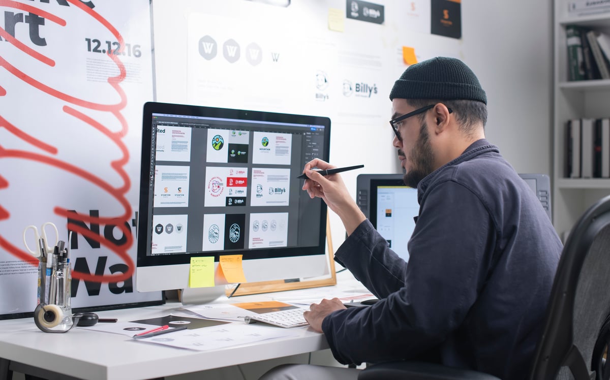 A professional holding a pen while looking at page layouts on a computer.