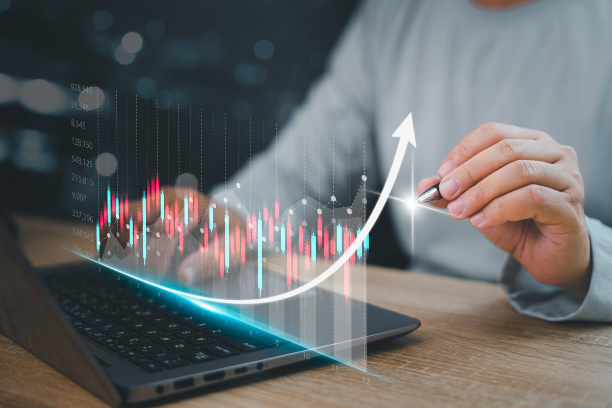 A hand tracing a holographic stock chart emerging from a laptop.