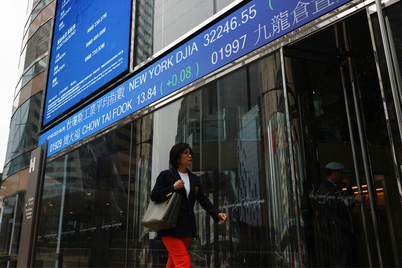 © Reuters. A woman walks past a screen displaying the Hang Seng Index at Central district, in Hong Kong, China March 17, 2023. REUTERS/Tyrone Siu/ File Photo