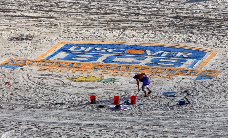 © Reuters. FILE PHOTO: An artist paints the sand on Ft. Lauderdale beach with the NCAA college football 2013 Discover BCS National Championship logo in Ft. Lauderdale, Florida January 6, 2013. REUTERS/Mike Segar/File Photo