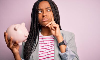 A person holding a piggy bank with a thinking or questioning expression on their face.