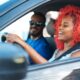 Two people smiling in the front seats of a car.